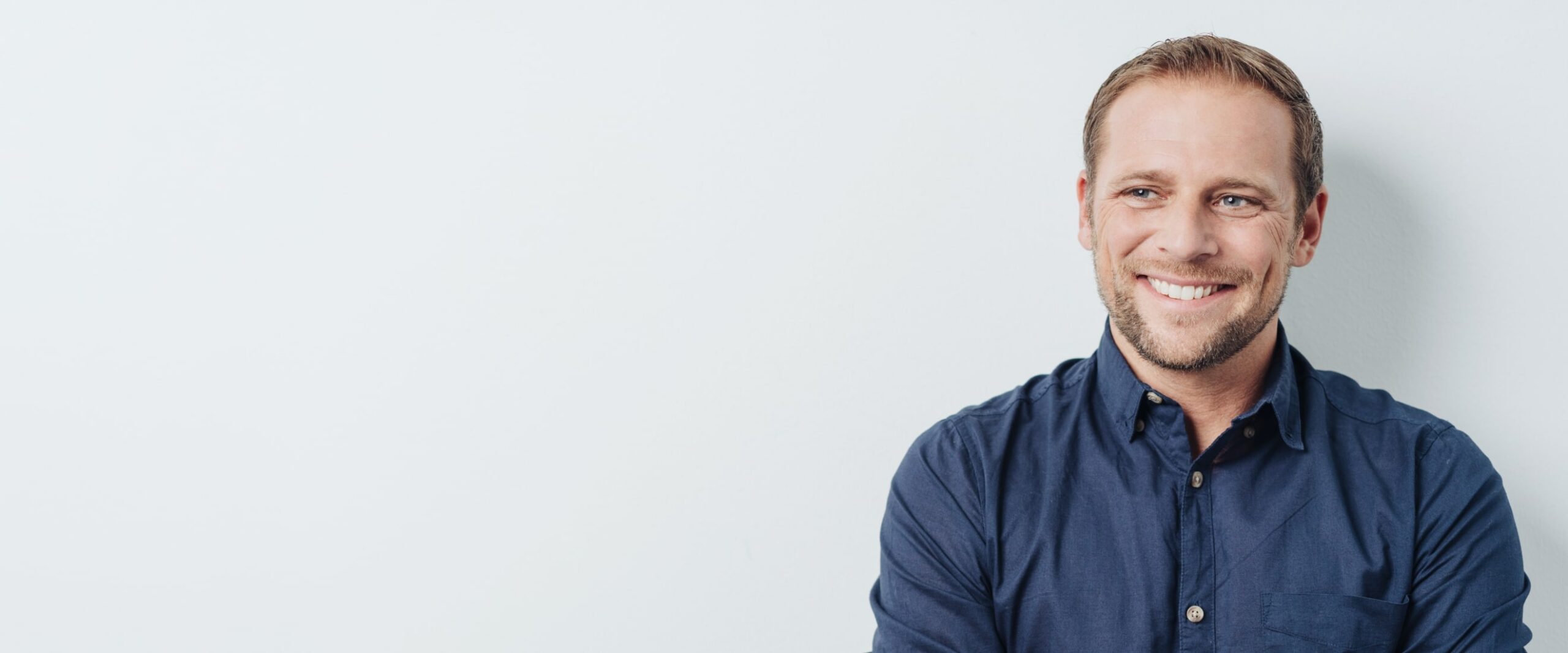 Smiling man in a blue shirt standing against a plain, light background