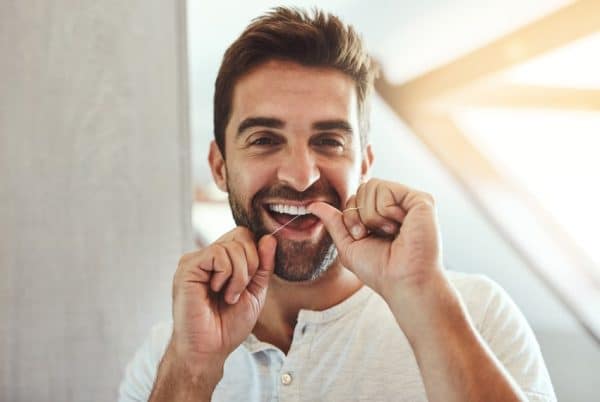 an adult man smiling and flossing his teeth